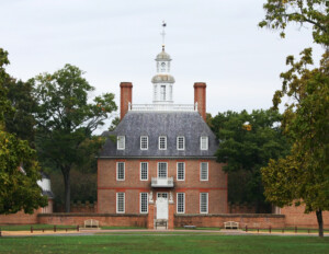 Chesapeake colonial style mansion with prominent windows and trim, exterior cornice, steep roof accompanied by railing, and two chimneys.