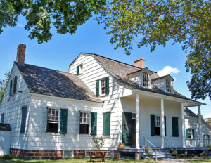 Dutch colonial house featuring two dormers, curved roof with steep slope, window mouldings with shutters, and shingle siding.