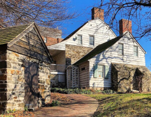 Dutch colonial style house with curved roof with steep slope, mixture of brick and shingle siding, along with window mouldings.