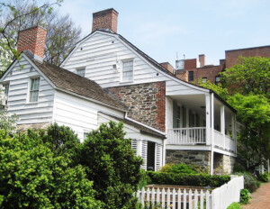 Dutch colonial style house with curved roof, mixture of brick and shingle siding, along with covered porch with columns, and window mouldings.