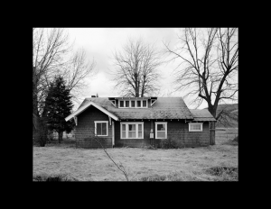 House that is dark in color, has a bungalow style overhang, and dormer style windows on the roof.