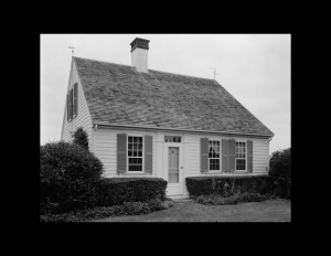 Cape cod style house with symmetrical appearance, shingle siding, and double-hung windows with shutters.