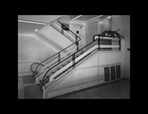 Interior of a building featuring an angular staircase with rounded art moderne railings, and shiny art moderne stone floors.