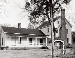 Old farmhouse style home with a full raised porch, shingle siding, and three chimneys.