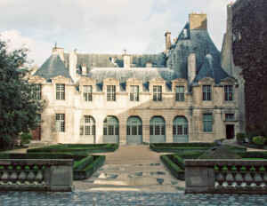 French city style brick exterior castle featuring window mouldings, door mouldings, sloped roof, and chimneys.