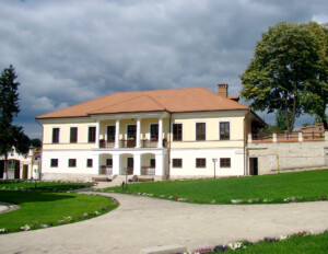 French colonial style house with stone, brick exterior, large second story window mouldings, and balcony porch with substantial balustrades.