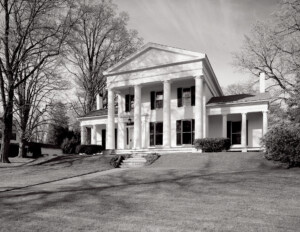 Greek revival style house featuring steps leading to the doorway, windows with shutters, huge pillar mouldings, and triangular roof.