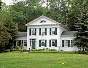 Greek revival style house featuring steps leading to doorway, doorway with mouldings and columns, and window mouldings with shutters.