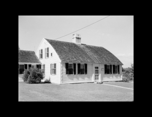 New england colonial style home with double-hanging windows with shutters, door mouldings, and a curved roof with a central chimney.