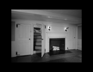 Interior of a new england colonial style room featuring fireplace mouldings, door mouldings, and a hardwood floor.