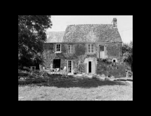 French country style house with brick exterior, mossy steep roof, one chimney, and window mouldings.