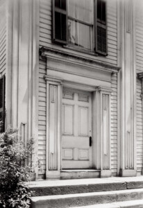 Exterior entrance door to the congressional church building, the door features columns, panel molds, and shingle siding around the door.