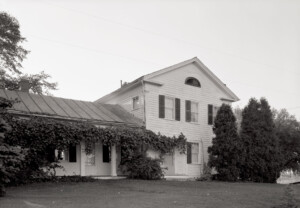 Updated exterior of Dirlam Allen House featuring covered porch with columns, windows casings with shutters, all painted in white.