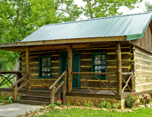 Log Cabin Style house with handcrafted logs, window mouldings, door mouldings, hangover roof, front covered porch with steps for entrance.