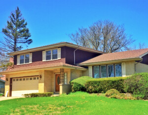 Mid-century modern style house with double hanging windows, shutters, overhanging roof, and a covered entrance that transitions into the garage.