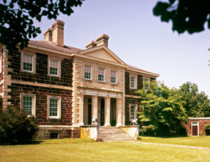 A side angle of a palladian style house featuring perfect symmetry, brick walls, window mouldings, cornice mouldings, and a covered entrance.