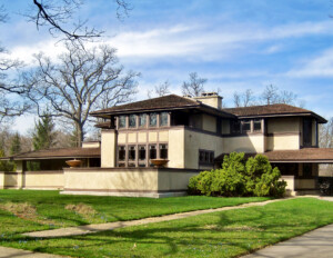 Prairie style house with low-pitched hipped roof, bank of window mouldings, horizontal banding, wide roof eaves, and stucco exterior.