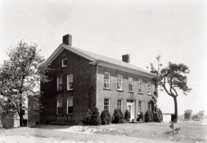 Exterior of Thomas Hurst House featuring front door with column detail, and panel molds, tall windows with shutters and brick chimneys on the roof