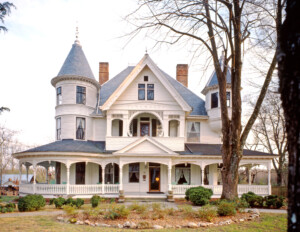 Victorian style castle with window mouldings and shutters, cornice mouldings, overhanging roof, and covered porch.