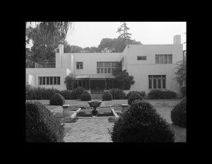 Asymmetrical international style building that has flat roof, roof porch on back, window mouldings, and a gated entrance.