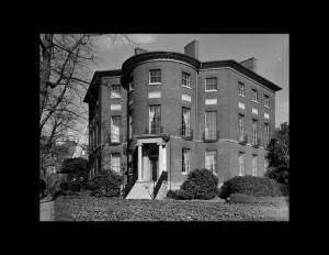 Octagonal plan style building with door mouldings, steps leading to door and tall window, normal window mouldings.