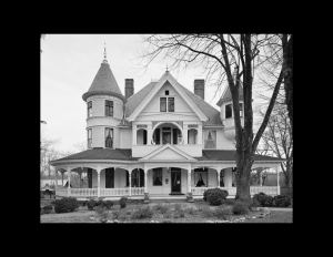 Exterior house with victorian style featuring a wrap-around porch, window mouldings, balcony on second floor, and conical towers on both sides.