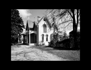 Exterior of gothic revival style castle with steep roof featuring pointed arch, large curved windows, and covered porch with columns.