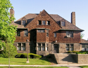 Shingle style house has the upper half with shingles, and lower half with stone, and also has window and door mouldings.