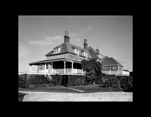 Giant shingle style building with balcony on second floor, high pitched hipped roof, and many dormers.