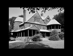 Shingle style building with balcony on first and second floor, high pitched hipped roof, and many window mouldings.