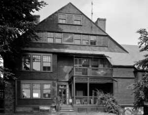 All wood shingle style house showcasing window mouldings, steep roof, first and second floor balconies, and door mouldings.