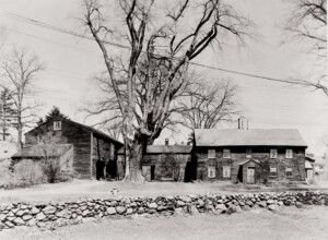 Exterior of Benjamin Abbott Farmhouse featuring shingle roofing, plaster on chimney, door mouldings, and window casing mouldings.